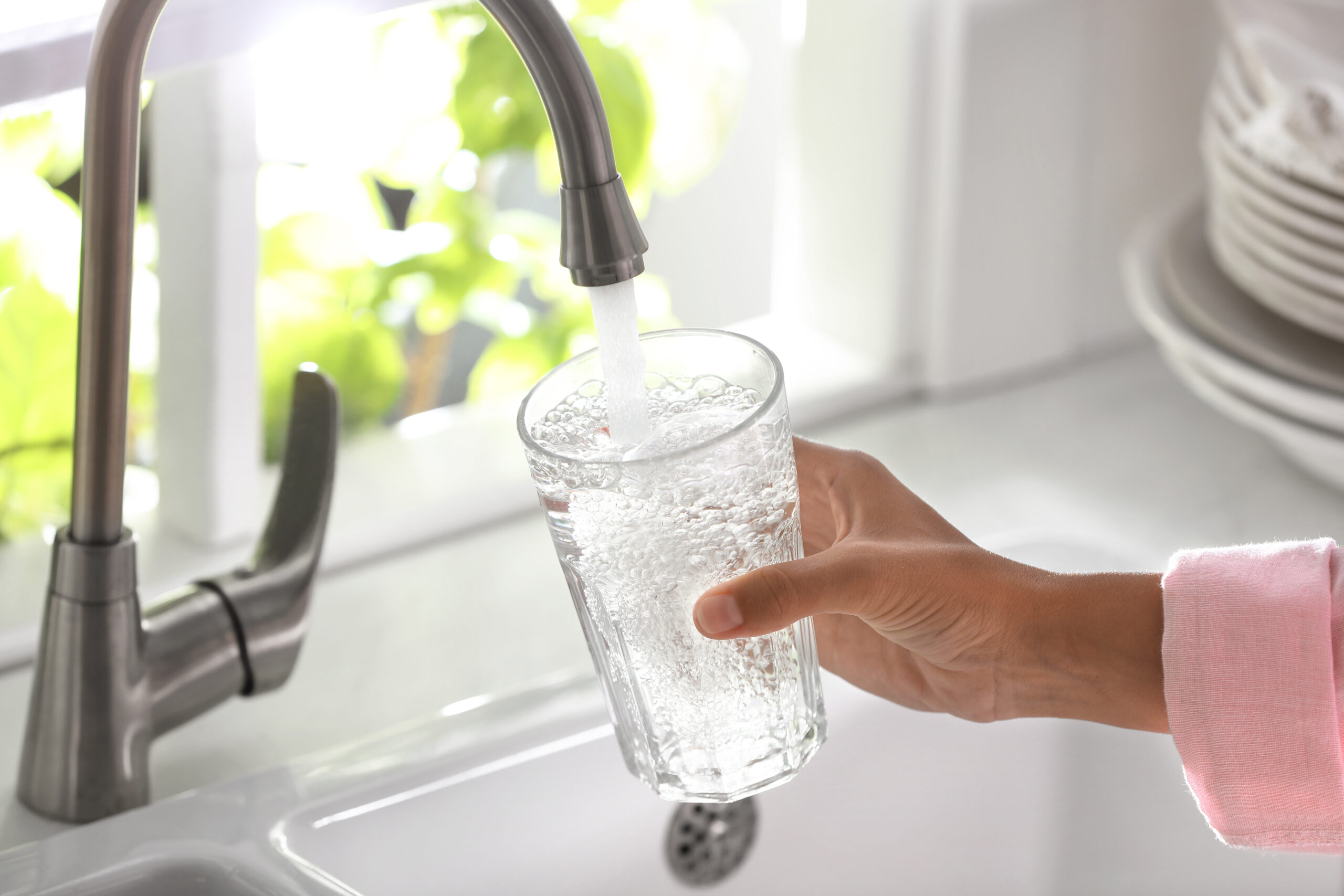 Hand filling a glass with water from a kitchen tap.