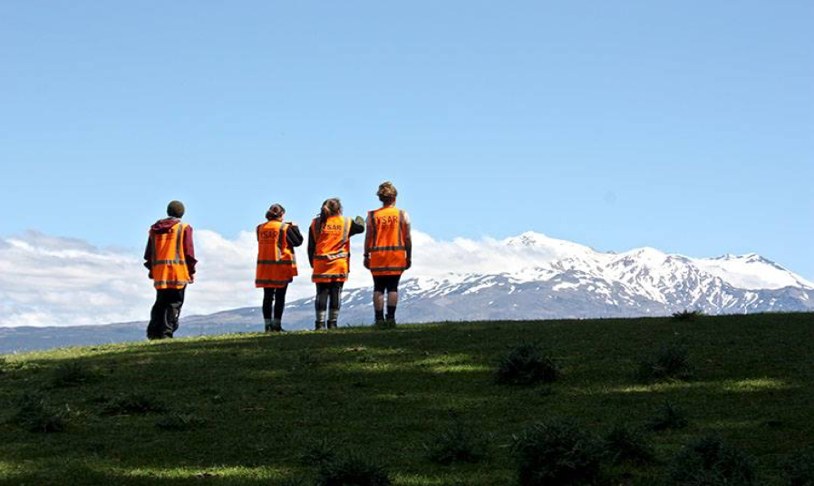 Four people in hi-vis vests overlooking snow-capped mountains.