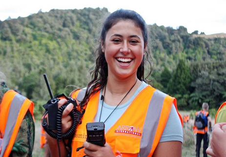Woman holding walkie-talkie wearing hi-vis smiles for photo.