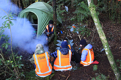 Search and rescue volunteers in hi-vis gathered around a tent in a forest.