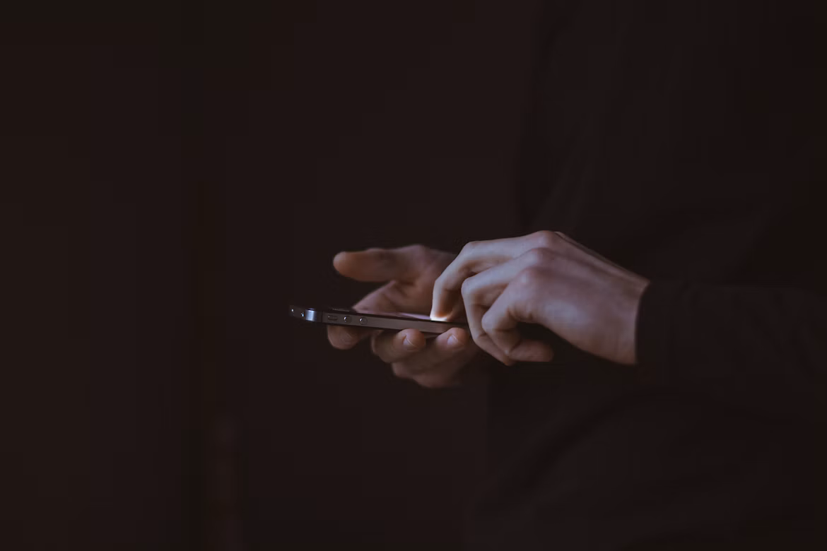 Close-up of hands holding and using a smartphone against a dark background.